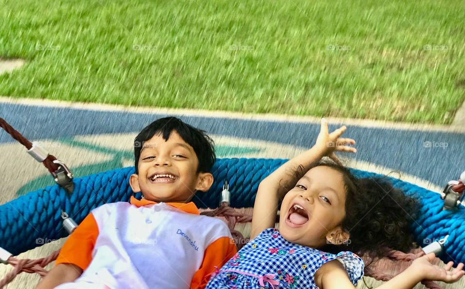 Kids enjoying our outdoor swinging and they both laugh very loudly.