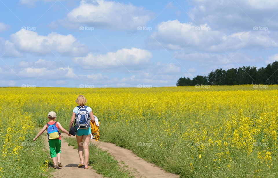 morning walking family woman and child boy rapeseed field blue sky clouds background