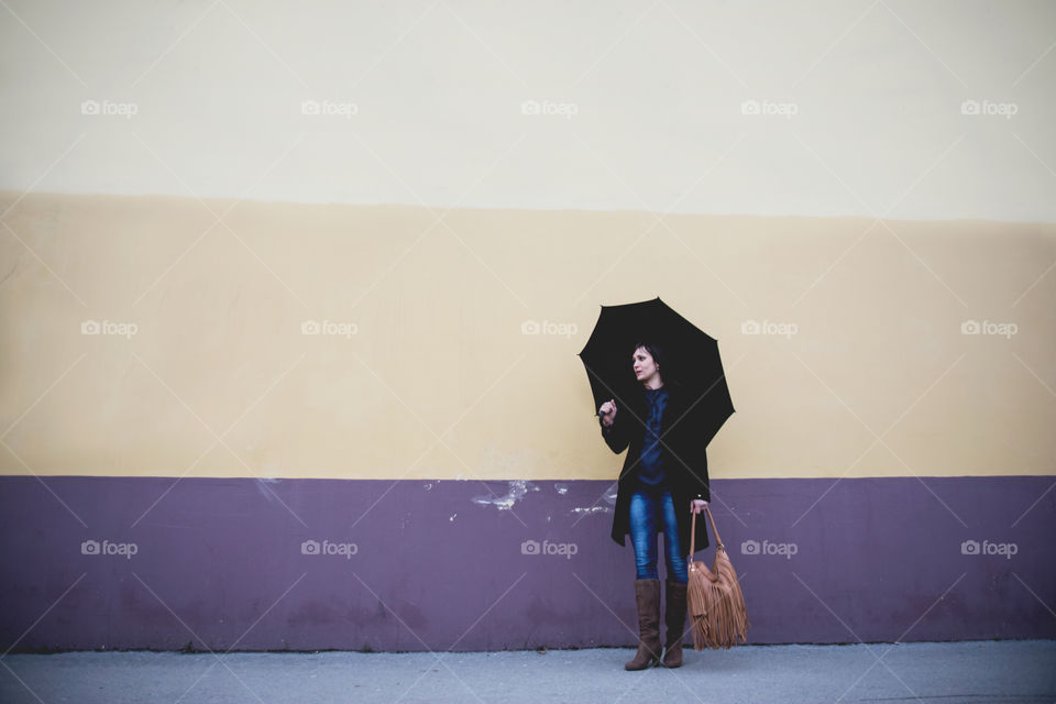 Woman standing near the wall with holding bag and umbrella