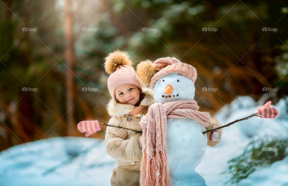 Little girl with snowman in winter park