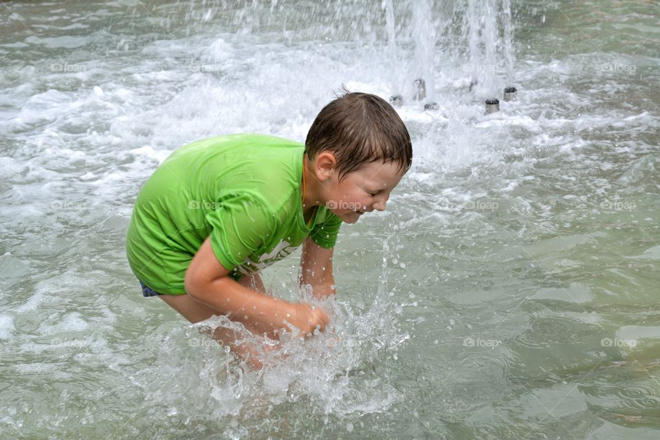 child boy in the water splash fountain, summer heat, city street view