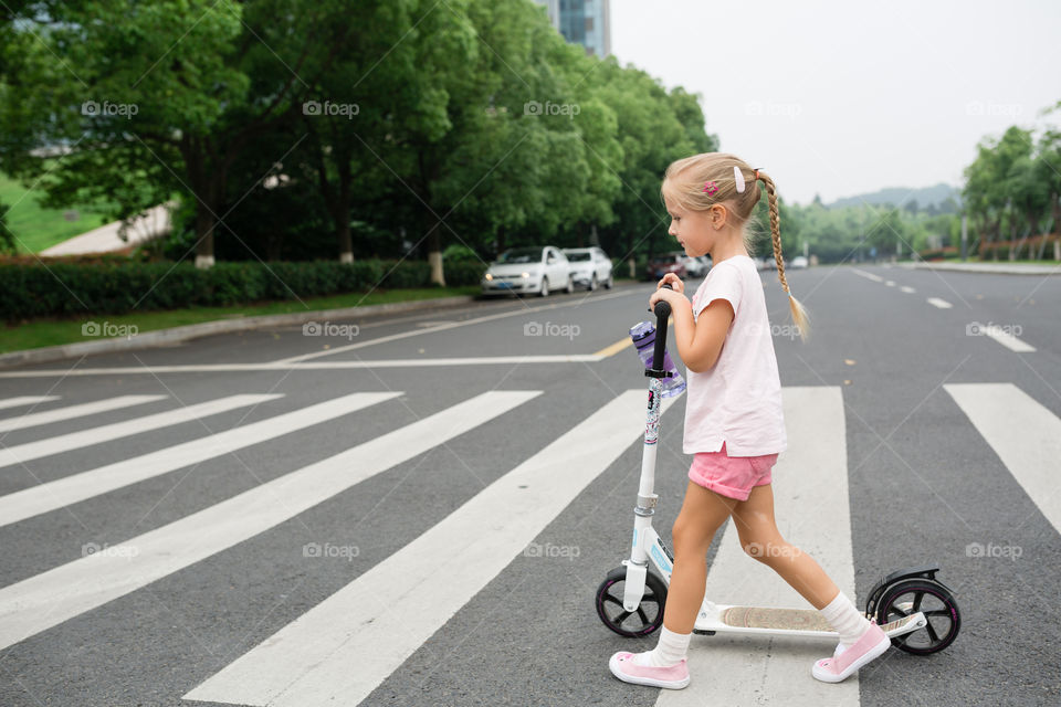 Little girl with blonde hair coming on pedestrian with scooter 