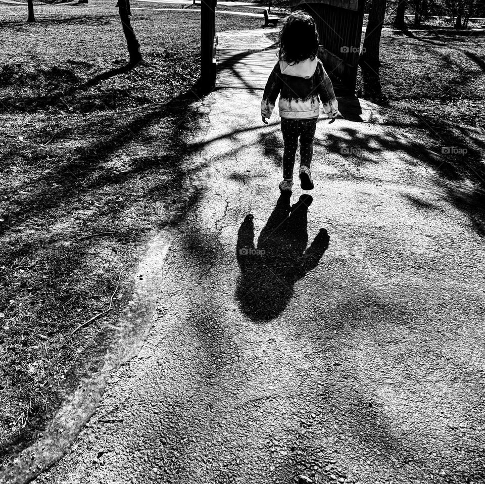 Black and white portrait of a toddler girl walking in park, toddler girl walks in park ahead of mommy, big shadow of a little girl, little toddler girl with a big shadow, black and white portraits, shadows in the park