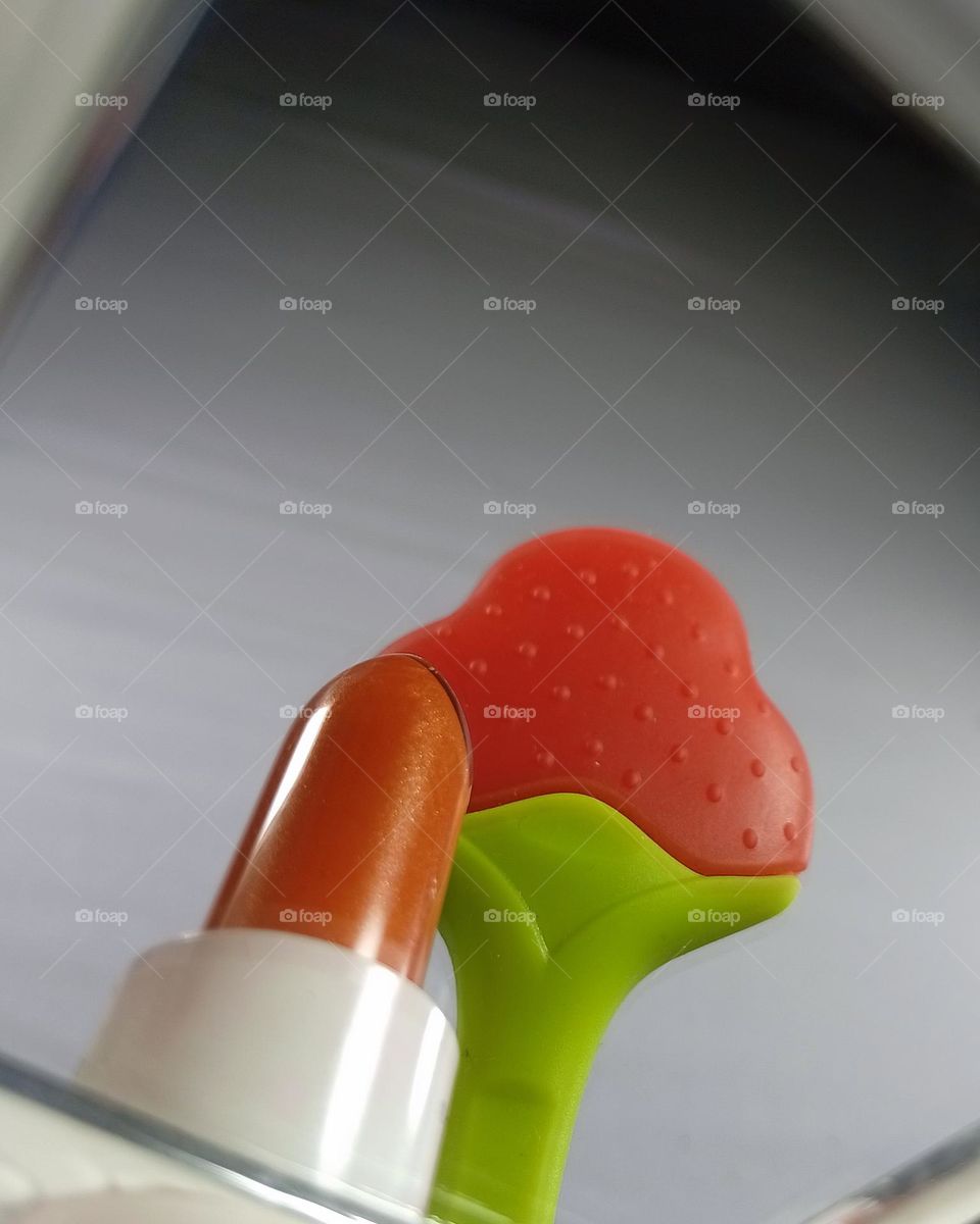 reflection of lipstick and baby teether. in the mirror