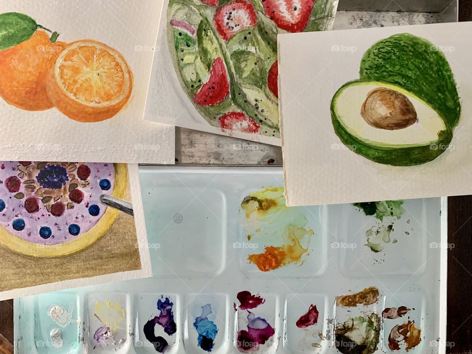 Overhead view of miniature watercolor paintings and metal watercolor palette with dried pigments 