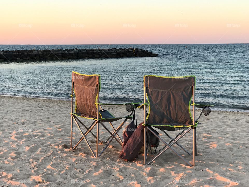 Two empty beach chairs facing the sea during sunset 