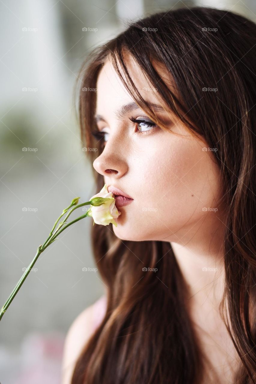 Close up portrait of beautiful girl. A flower near the lips