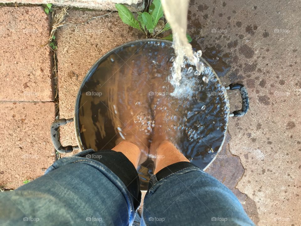 Water pouring from water faucet over bare feet in bucket pail