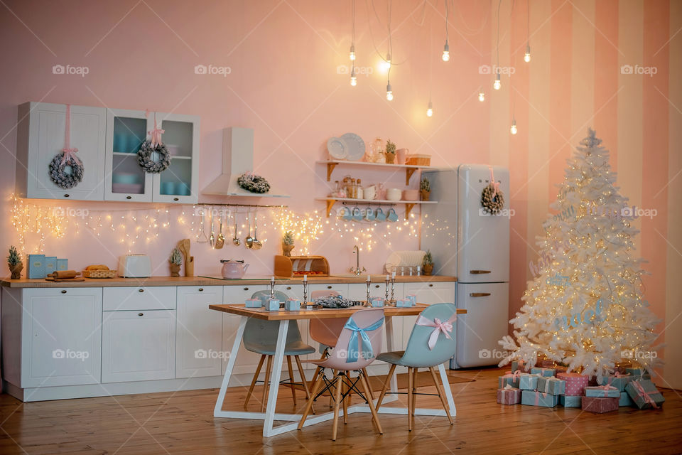 Festive winter cozy kitchen interior with garlands, decorations and gifts.  Christmas dinner at the decorated table.