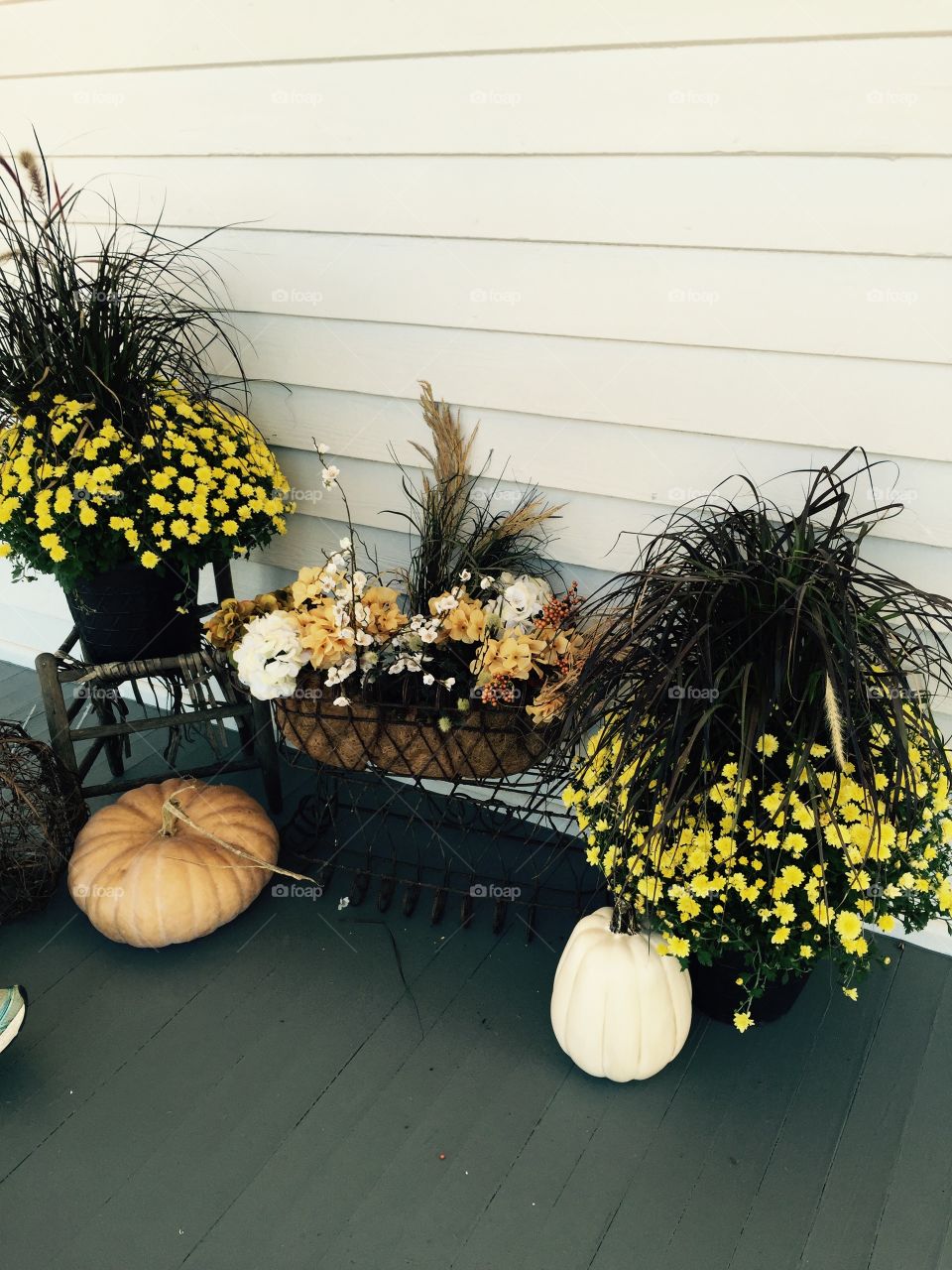 Yellow mums, gourds, and fall decorations on a porch. 
