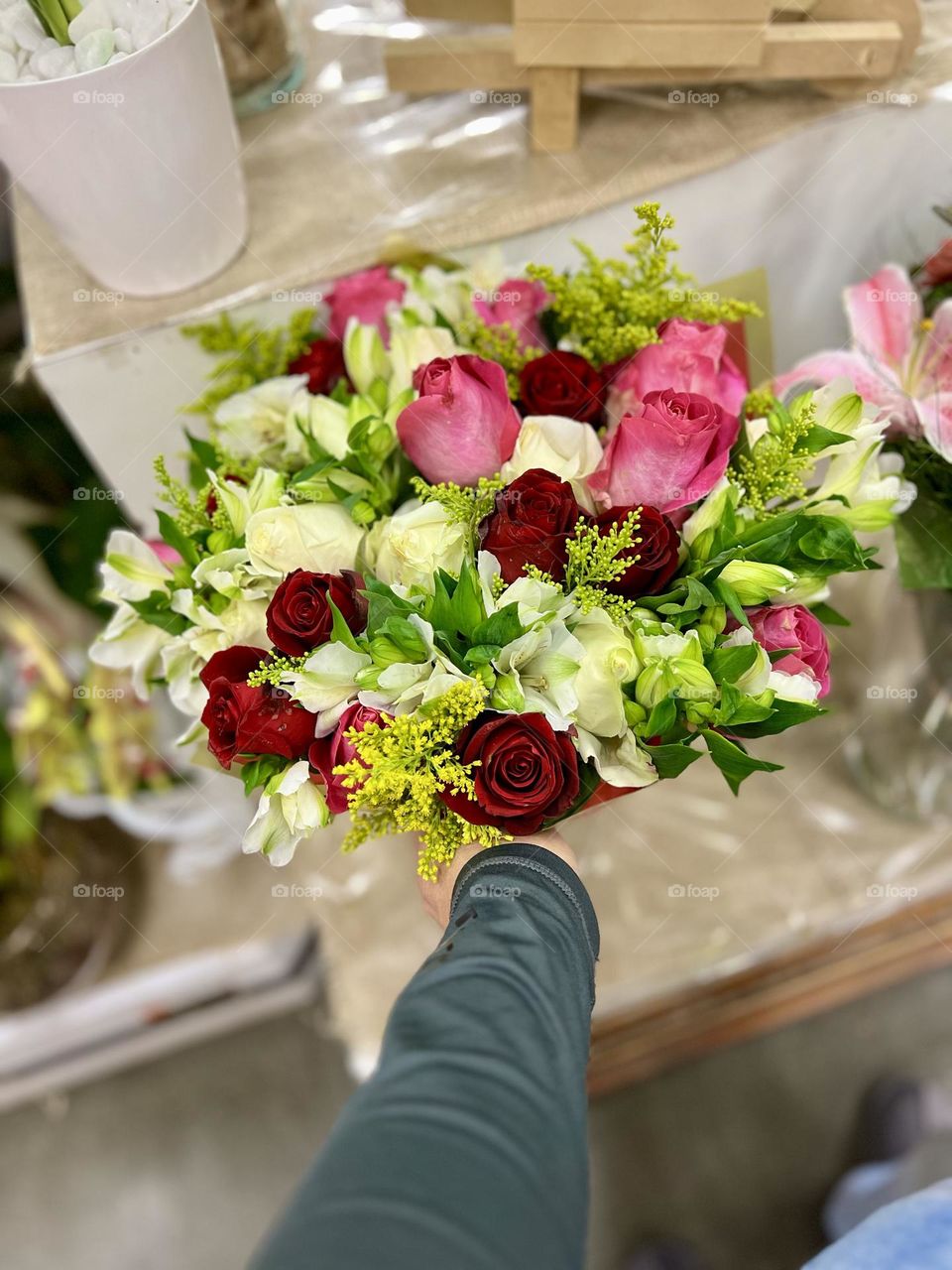 A beautiful bouquet of mixed flowers, including red roses, light roses and white flowers. The image captures the hand of a person holding the floral arrangement, suggesting joy and celebration.