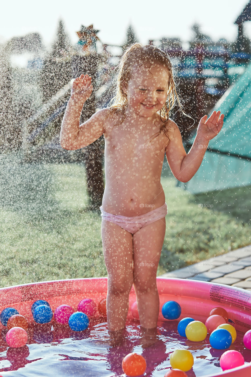 Little cute adorable girl enjoying a cool water sprayed by her father during hot summer day in backyard. Candid people, real moments, authentic situations