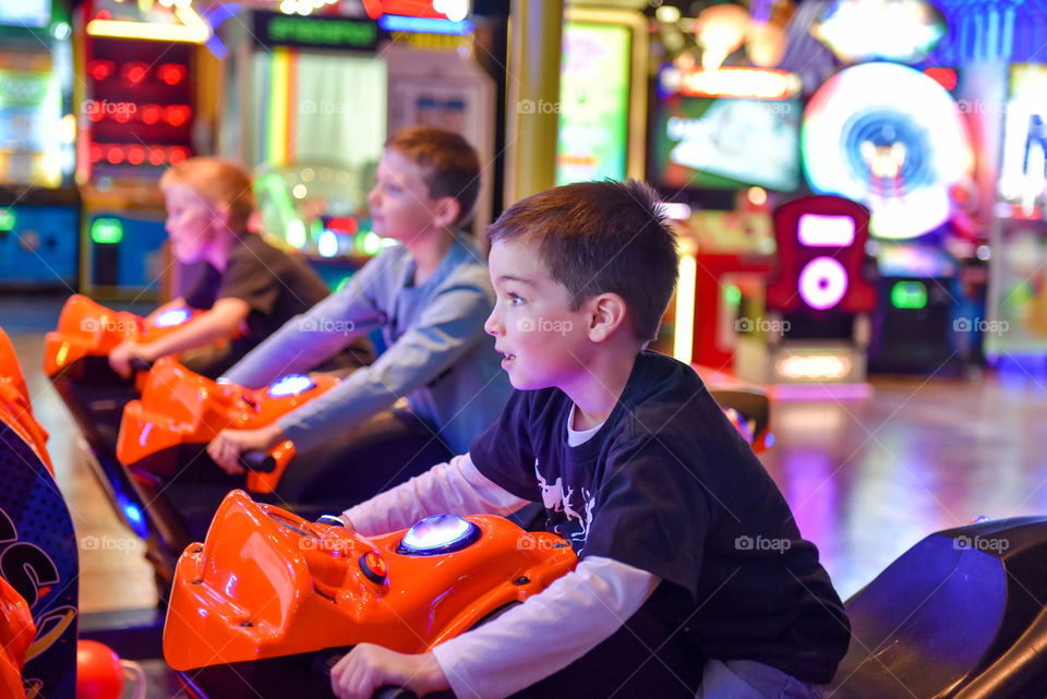 Young boy's face illuminated by the glow of a racing game at an indoor arcade