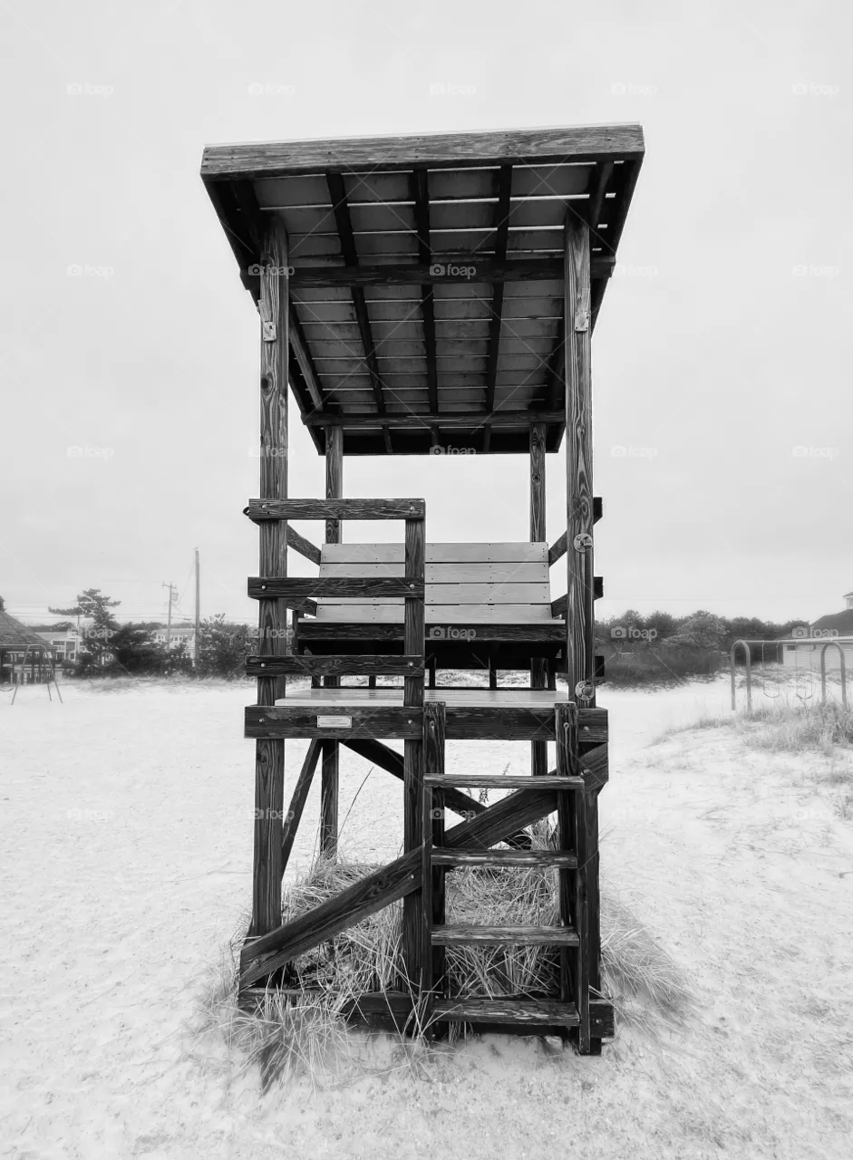 Black and white photo of an empty lifeguard stand on the beach in wintertime.  Stark, focus on foreground, mental health concept 
