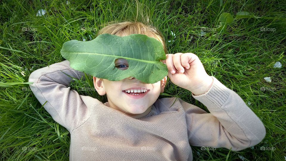 little boy with a leaf on his face is lying on the grass