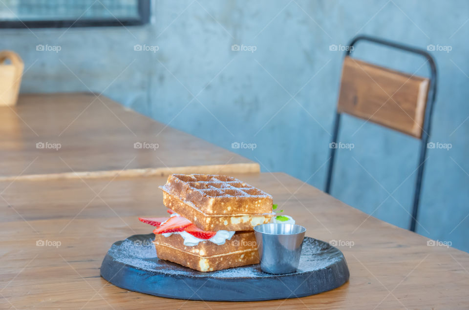 Waffle Strawerry fresh cream in the black plate on wooden table.