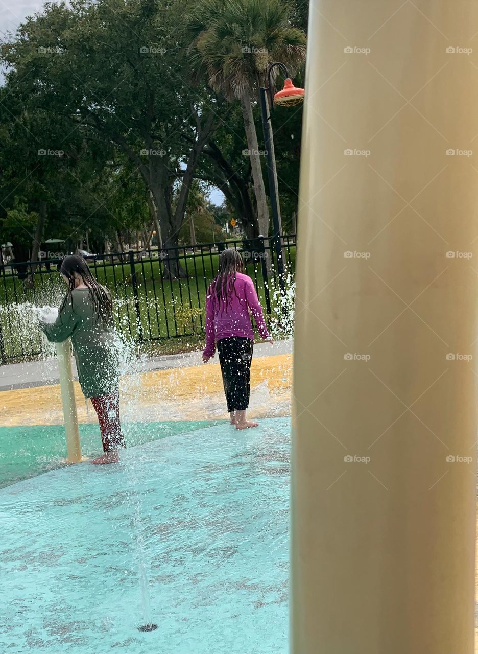 Children having lots of fun in the water at the colorful kids splash pad at the city park for children during a really warm day in Florida.