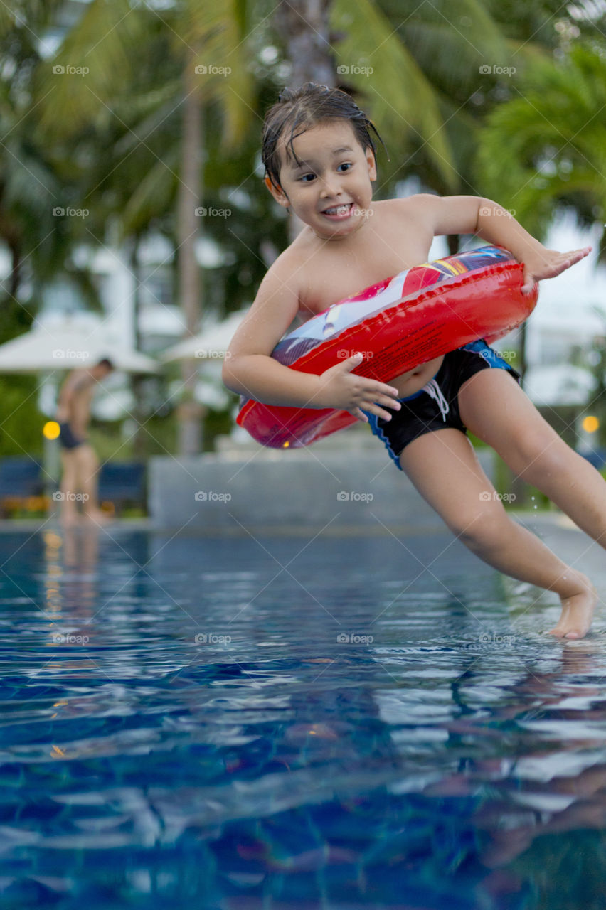 happy young boy jumping into the pool during summer