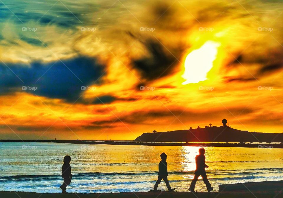 Brothers Against The Sun. Three Brothers Walking Across A Beach During The Golden Hour
