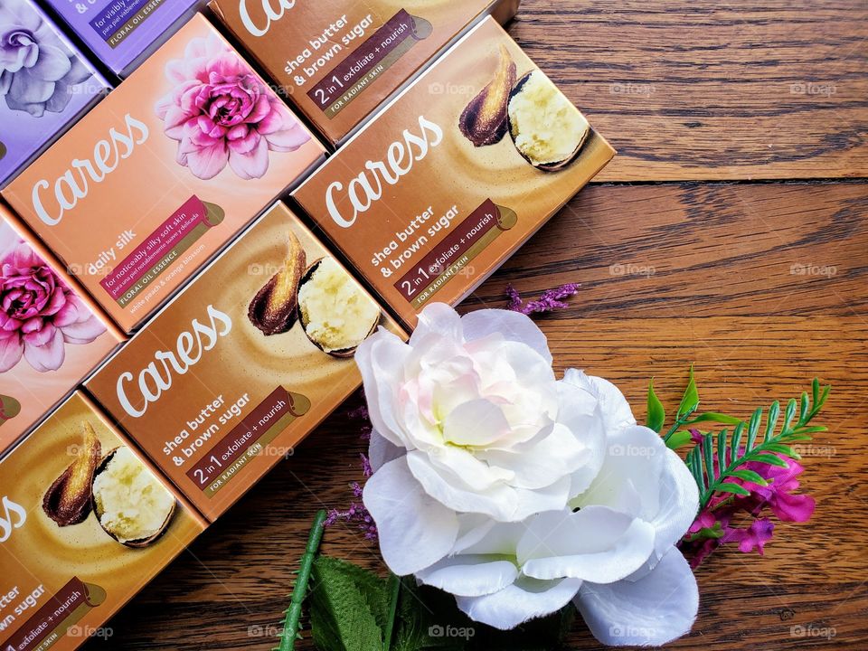 The new look Caress bar soaps on a wood surface accented by a white flower.