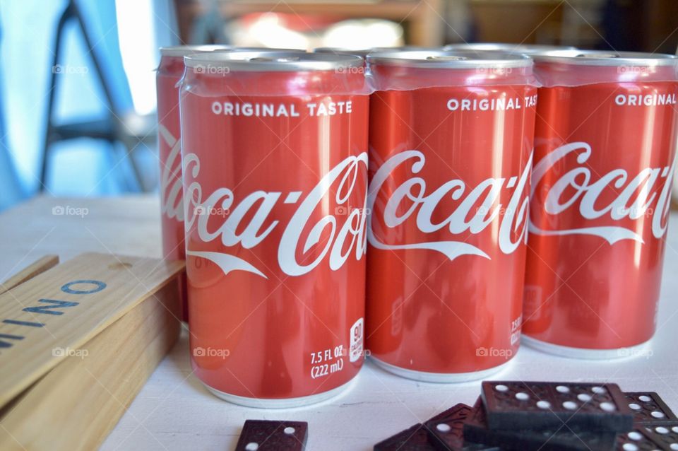 A six pack of Coca-Cola cans with dominoes