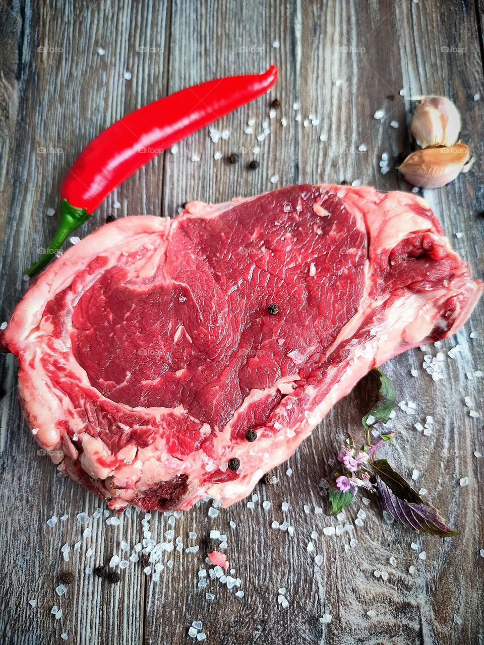 Healthy food. Meat is a source of natural amino acids. On a wooden surface is a piece of beef steak, red chili pepper, white salt, peppercorns, garlic cloves and a sprig of basil