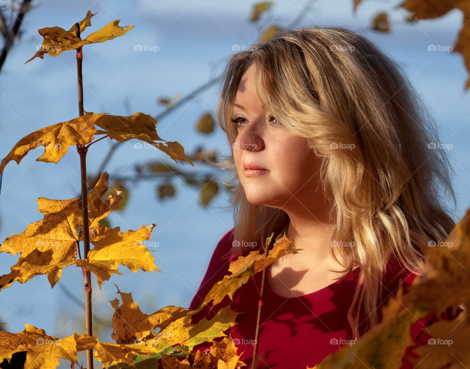 Portrait of a young woman with blond long hair sitting thoughtfully against the background of the golden leaves of autumn trees on a sunny September evening