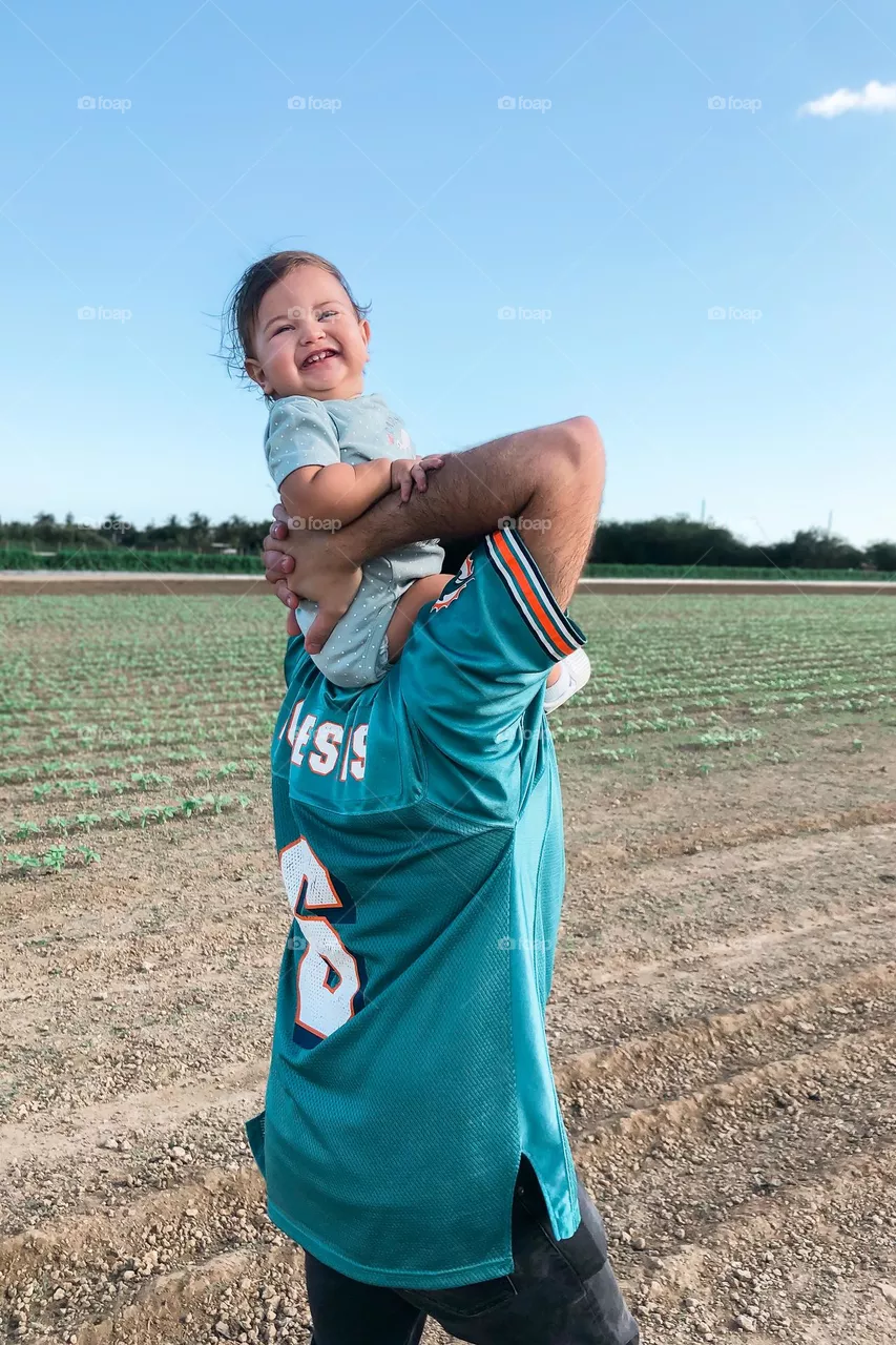 Loving father holding his overjoyed, happy baby on his shoulders as they stroll through a strawberry field.