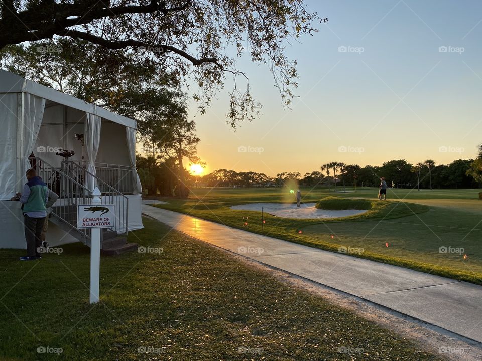 The sun sets over a beautiful golf course. The sign warning of alligators sits in the foreground.