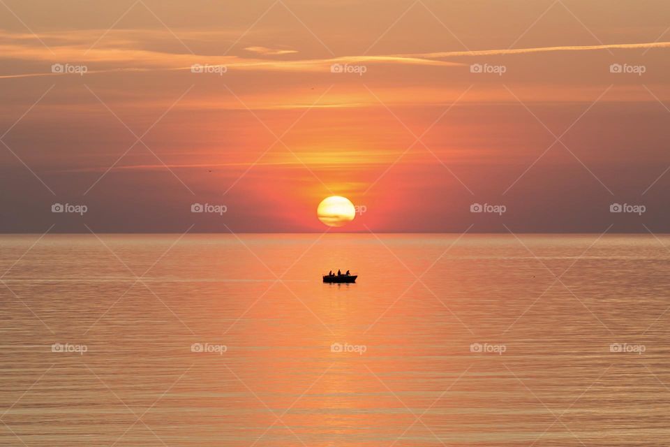 Orange colored sunset with reflection in the ocean, silhouette of a little boat 