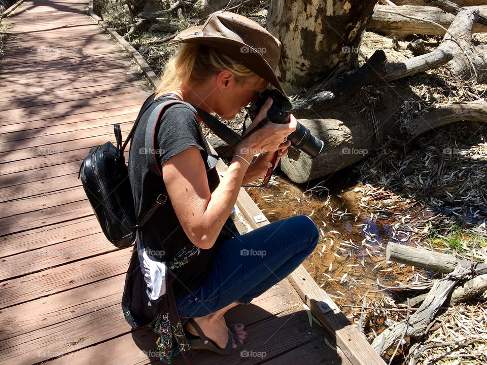 Female photographer kneeling wearing leather hat shooting photograph outdoors nature 