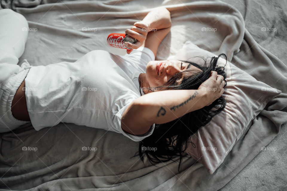 the girl lies on the bed and holds a Coca Cola