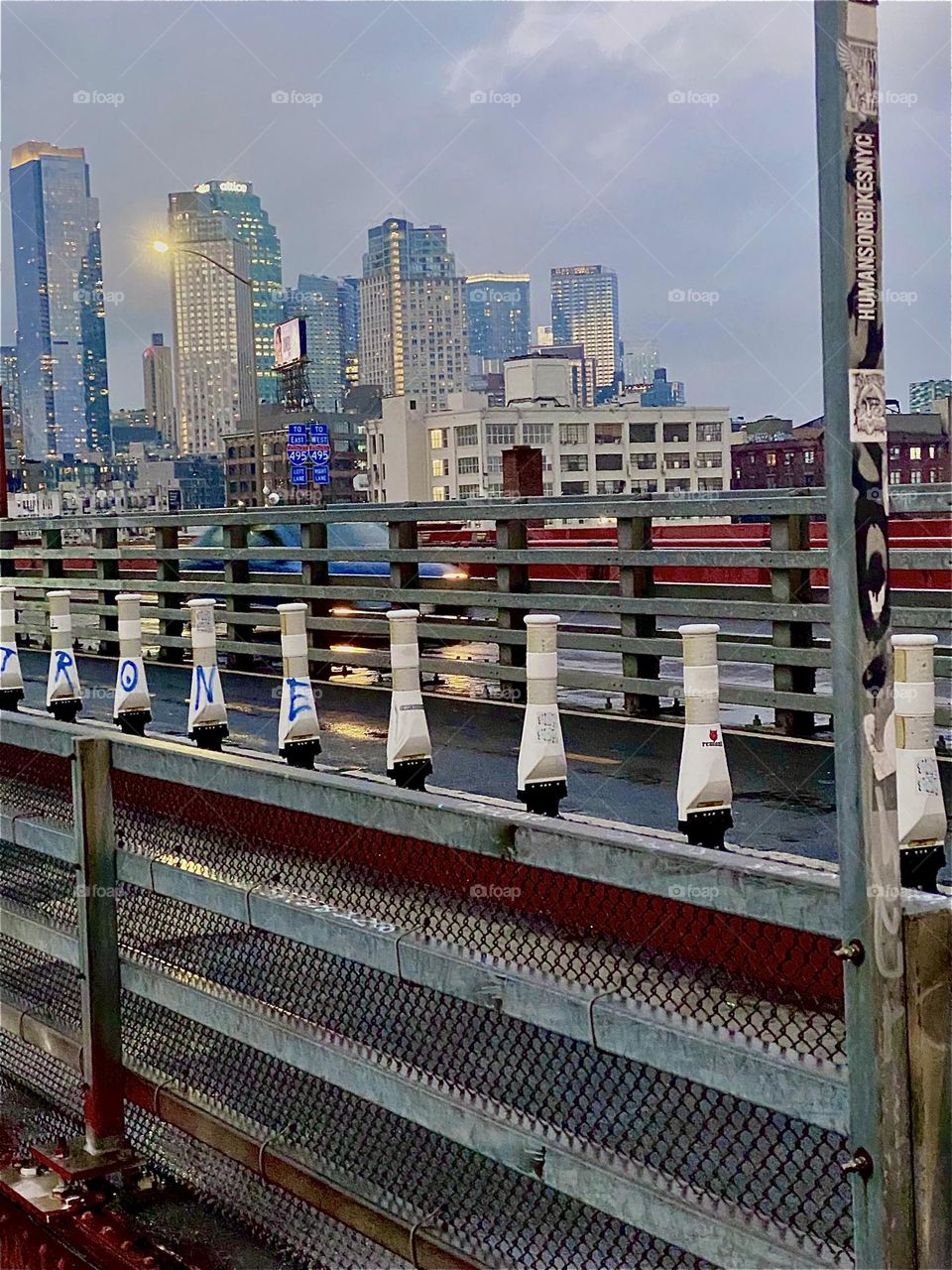 This is the „Pulaski Bridge“ seen walking towards LIC, Queens. The railing that separates the lanes creates a strong streamlined effect and clusters of high rise buildings pick up the sun‘s last setting rays. 2023. Hypnotic Productions