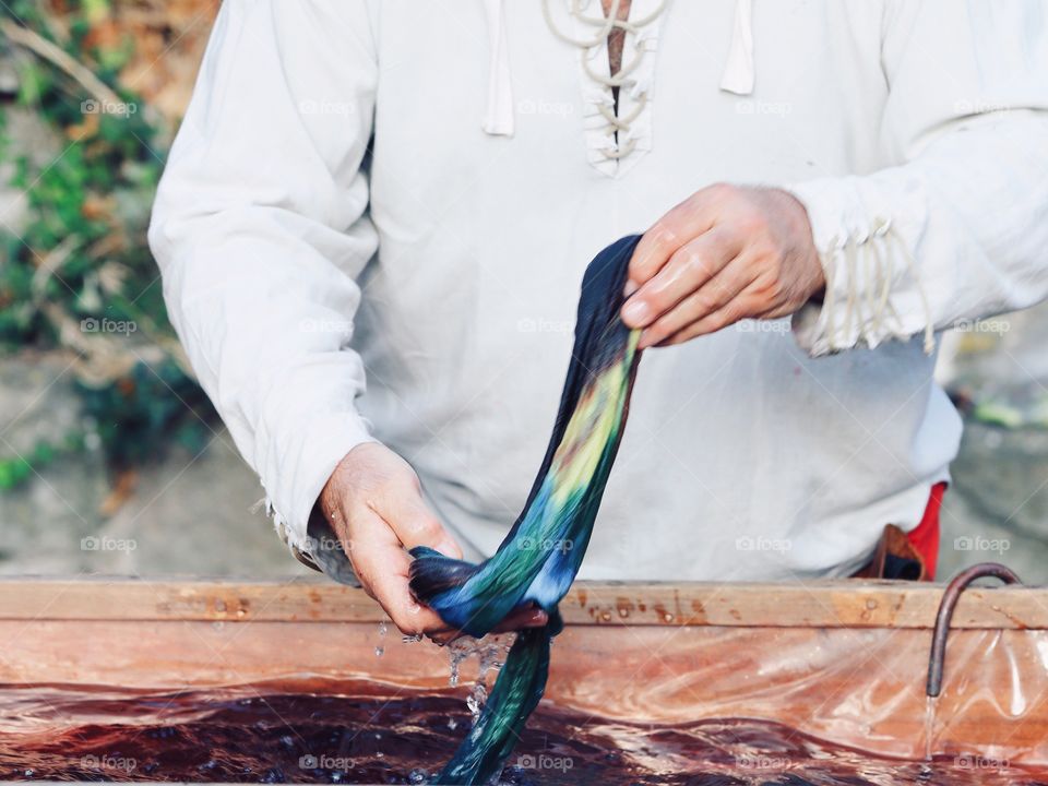 The man in the old national costume is showing a process of the hand dyeing fabric in Italy