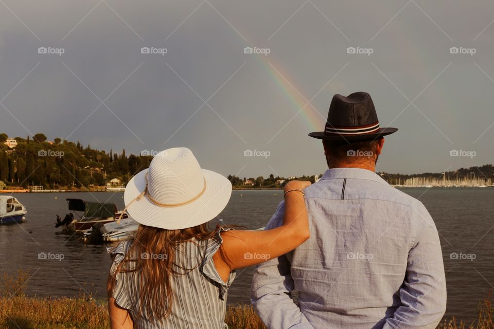 A woman and man watching sea and rainbow