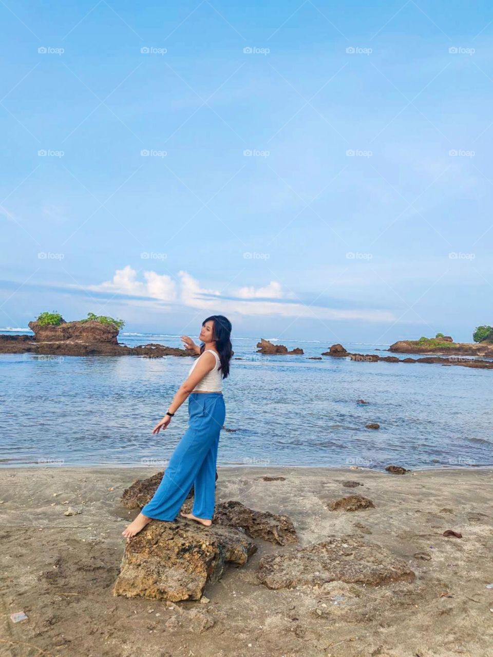 Portrait of a young woman standing on a rocky beach cheerfully