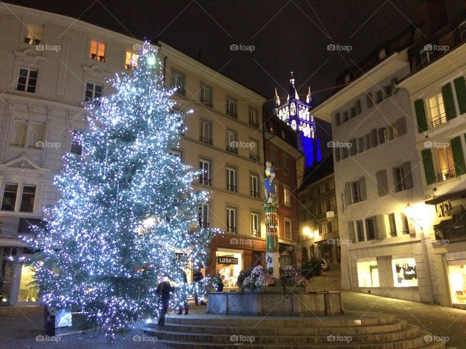 Brightly lit giant Christmas tree in front of church tower in Geneva’s Old Town.