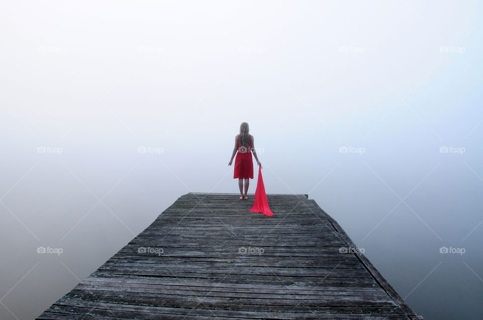 girl in red dress with red scarf on grey foggy pier