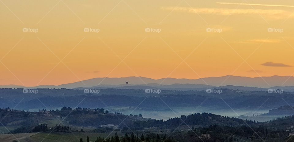 Sunrise over the Tuscan countryside with a hot-air balloon hovering over the morning mist in the valleys below - taken outside San Gimignano, Italy