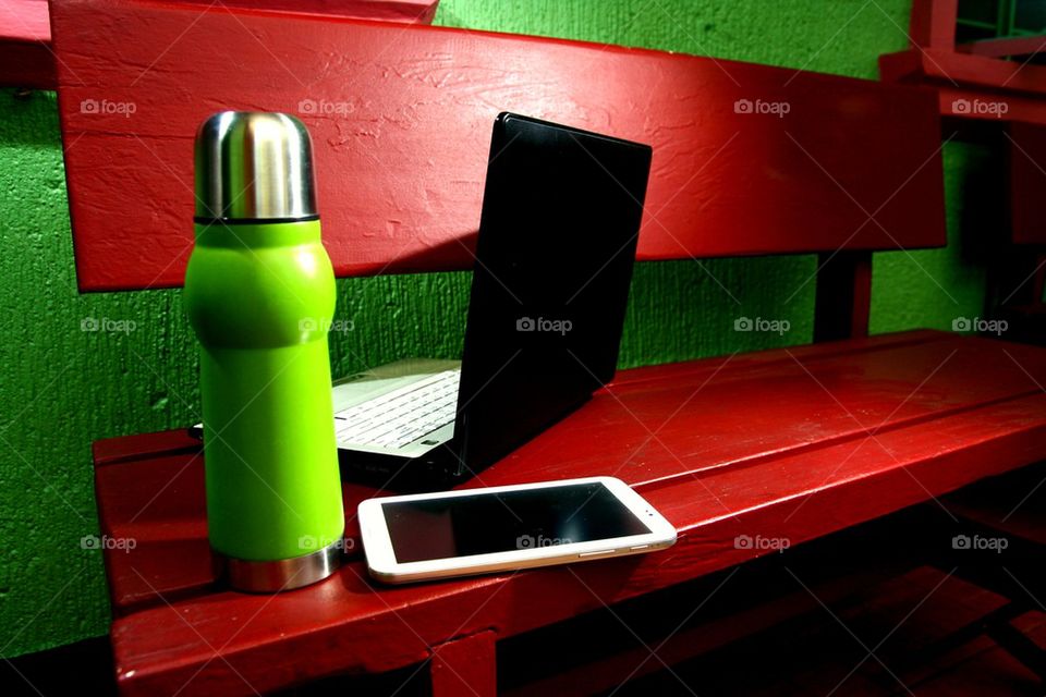 flask, tablet and laptop computer on an outdoor bench