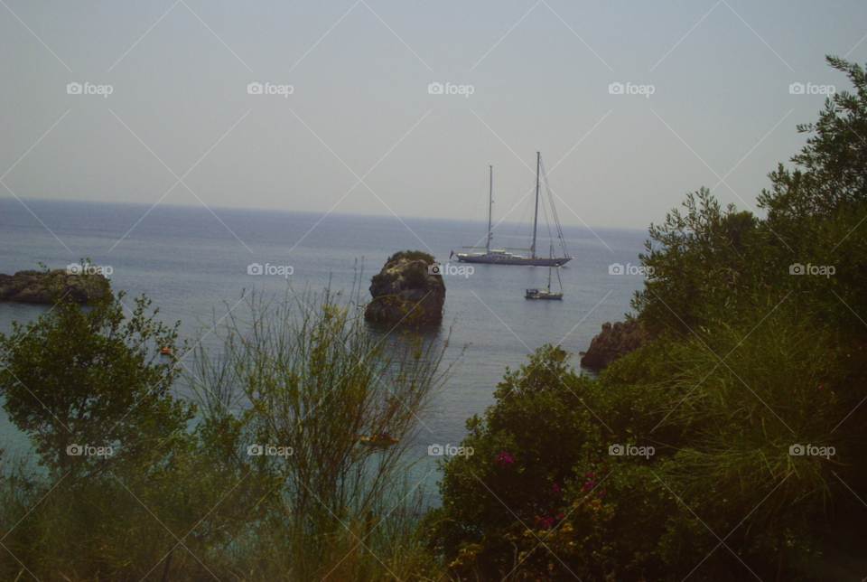 yacht moored in cove overlooking from top of cliff walk. mediterranean sea. off greece. by pawright68