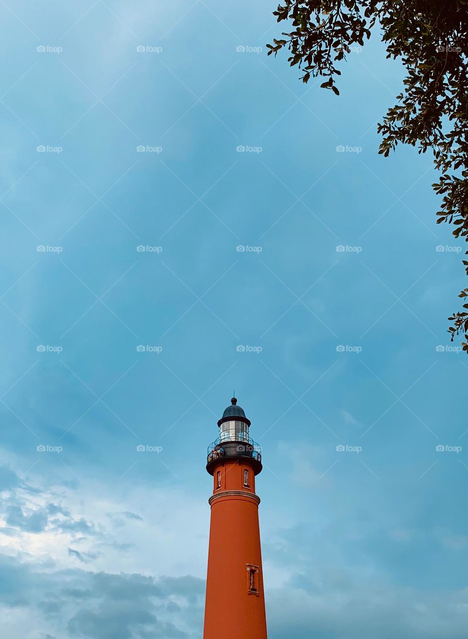 Ponce Inlet Lighthouse, also called the Mosquito Inlet Lighthouse. The current tower was lit in 1887 and stands 175 feet tall, making it the tallest lighthouse in Florida, third in the USA. Top seen with tree branches and leaves on the foreground.